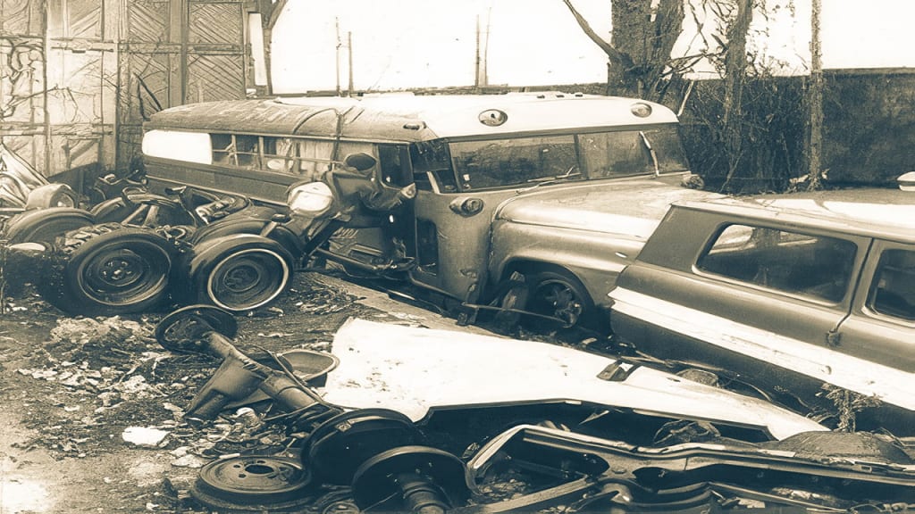 An old school bus and wrecked cars in a junkyard.
