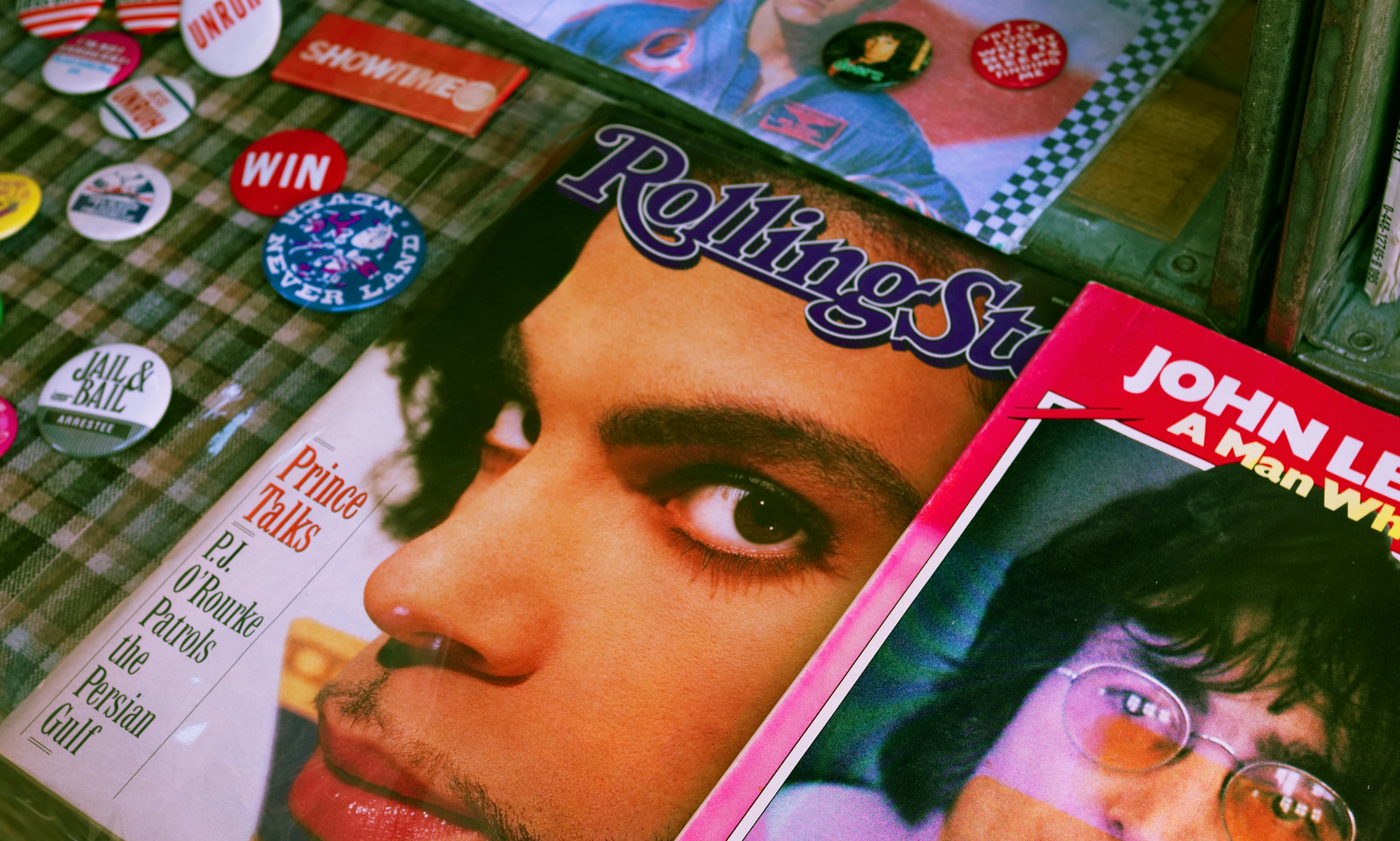 A stack of vintage magazines and pin badges, including a Rolling Stone cover, from the era of the story